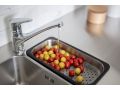 Detajl kuhinjskega pomivalnika z inox koritom in kromirano armaturo, iz katere teče voda v perforirano posodo za odcejanje; v njej so oprani rdeči in rumeni češnjevi paradižniki.