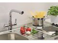 Detajl kompaktne inox kuhinjske enote z armaturo, odcejalno površino in električno kuhalno ploščo; na plošči je lonec s testeninami, ob njem pa paradižniki, česen in bazilika.