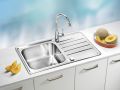 Inox kuhinjsko pomivalno korito z eno posodo in rebrasto odcejalno površino ter kromirano armaturo, vgrajeno v svetel kuhinjski pult; ob njem sta narezana melona in rezine sadja.