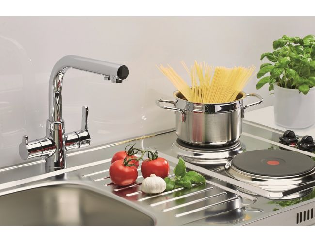 Detajl kompaktne inox kuhinjske enote z armaturo, odcejalno površino in električno kuhalno ploščo; na plošči je lonec s testeninami, ob njem pa paradižniki, česen in bazilika.