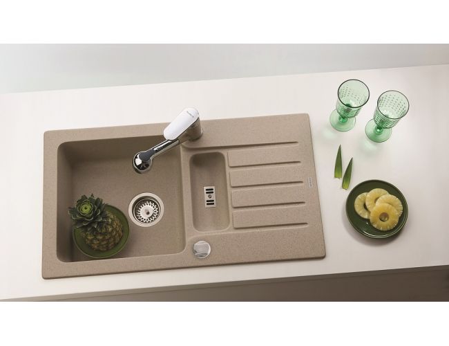 Kuhinjsko korito iz kompozitnega materiala v bež barvi z elegantno armaturo in odcejalnikom, obkroženo s stilskimi dodatki.