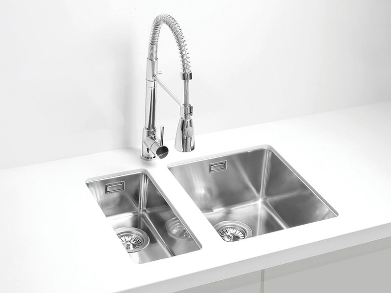 Inox kuhinjsko pomivalno korito z dvema posodama ter visoko vzmetno armaturo s tušem, vgrajeno v bel kuhinjski pult.